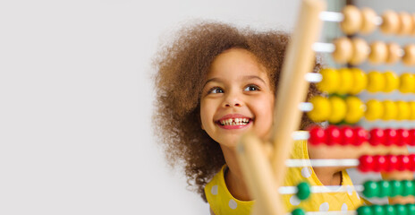 banner of A Black student in a yellow dress laughs brightly behind a colored abacus in an elementary school - obrazy, fototapety, plakaty