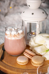 Obraz na płótnie Canvas A glass of hot cocoa with marshmallows, macaroni cakes and white tulips on a tray in bed close up, vertical photo. Cozy spring home concept