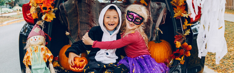  Trick or trunk. Children celebrating Halloween in trunk of car. Boy and girl friends celebrating October holiday outdoor. Social distance and safe alternative celebration. Web banner header.