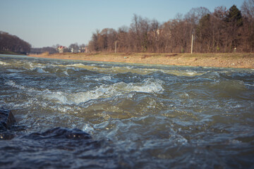 Water texture. Mountain river on the background of the city. Waves of green, blue and gray. Calm and tranquility. River shore. Rapid flow of water, photo of the surface of the river