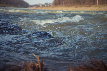 Water texture. Mountain river on the background of the city. Waves of green, blue and gray. Calm and tranquility. River shore. Rapid flow of water, photo of the surface of the river
