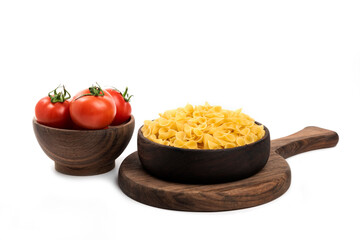 A wooden bowl full of fresh juicy red tomatoes with bow pasta on a wooden board