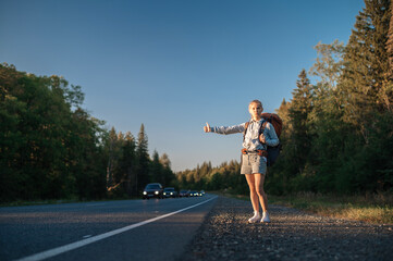 Travel woman with backpack hitchhiking on road