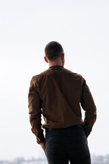 A young successful male businessman stands loosely near a large window and looks out over the city.