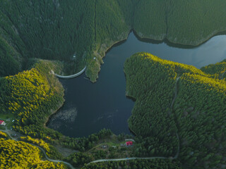 Aerial drone view above Gatu Berbecului lake at sunset. The water is hold by an arched concrete dam, built within the wilderness of Cindrel Mountains. Carpathia, Romania.