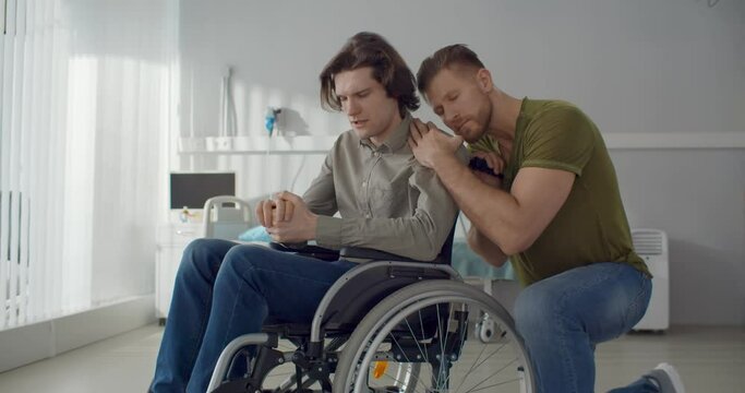 Young man hugging and supporting depressed boyfriend in wheelchair