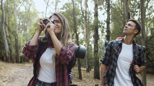 Happy hikers with photo camera taking pictures of landscape, while walking on forest path, talking, enjoying outdoor vacation and healthy recreation. Adventure travel concept