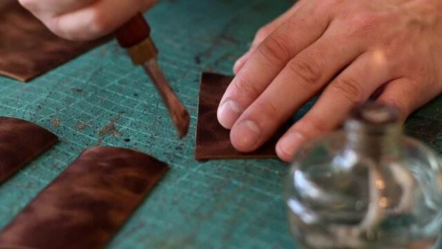 The process of manufacturing a leather cardholder.Processing the edges of leather workpieces with crimping tool.Leather handicrafts.Hobby concept.Artisan's hands close-up, slow motion.
