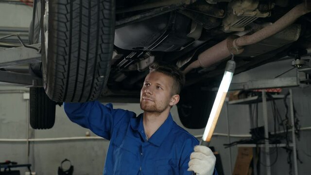 car mechanic examining car suspension of lifted automobile at repair service station with light transmission