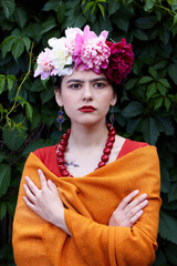 Girl brunette with red lips and a wreath of peonies on his head in the ethnic image of Mexican artist Frida Kahlo