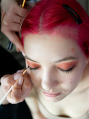 a pink-haired girl makes an eyeliner with an eyelash brush, close-up, top view