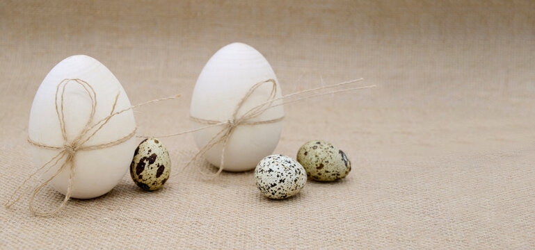 Two wooden eggs with twine bows, guail eggs on a burlap background. The concept of Easter, birth.
