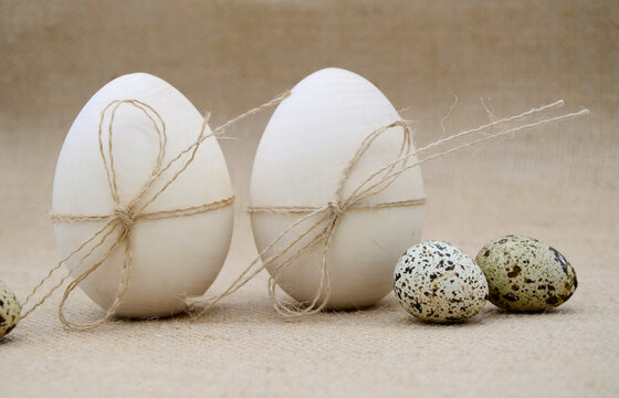Two wooden eggs with twine bows, guail eggs on a burlap background. The concept of Easter, birth.