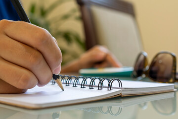 hand holding pencil, making notes in spiral notebook