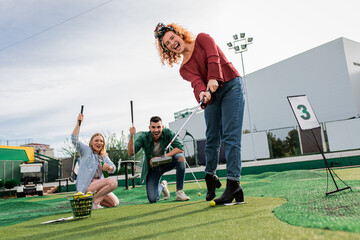 Group of smiling friends enjoying together playing mini golf in the city.