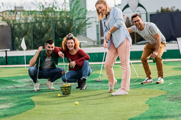 Obraz premium Group of smiling friends enjoying together playing mini golf in the city.