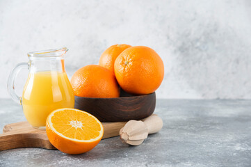 A wooden bowl of fresh orange fruits and a glass pitcher of juice