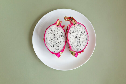Pitahaya Dragon Fruit fresh half cutted, served on a white plate. Pitaya with white pulp and balck seeds on pale green background.