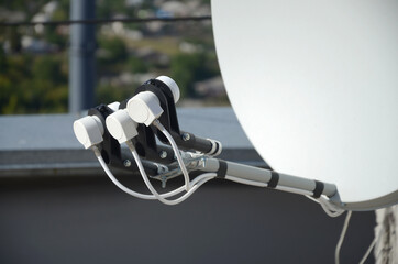 White satellite dish with three converters mounted on residental building rooftop concrete wall....