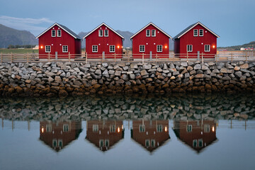 classic red fishing cottages in perfect symmetry sitting along a stone jetty with a slightly blurred reflection. Classic red houses of northern norway