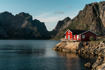 A single classic red cabin on the Islands of Lofoten. Perfect light shining on the bright red exterior with a beautiful mountain backdrop