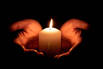 Due mani che tengono una candela accesa su uno sfondo nero. condoglianze. vista frontale