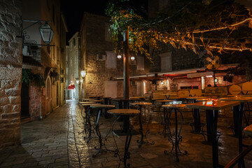 Empty street cafe terrace with tables and chairs in an old town of Budva at night, Montenegro.
