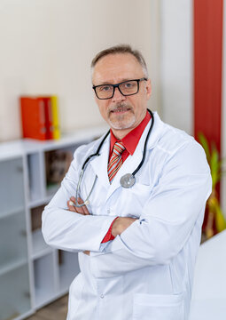 Portrait Of A Doctor Or Medical Specialist. Vertical Portrait. Man In Scrubs Standing Cross Hands In Ofice.