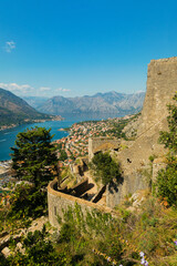 Colorful landscape with old walls in ancient citadel, sea, mountains, blue sky. Top view of Kotor bay from medieval fortress