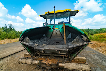 New road. Sidewalk machine paving fresh asphalt or bitumen on top of a gravel base during highway...
