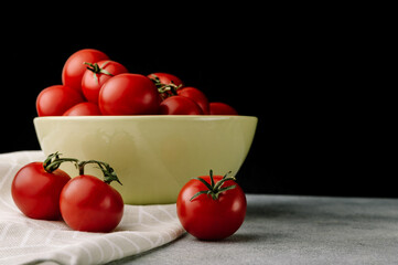 Red tomatoes with leaves in the bowl on dark background