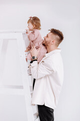 stylish man is having fun with cute child baby girl in decorated studio. daughter tries to climb the ladder. Love parenthood childhood concept. father's day, love care, deep devotion relationships