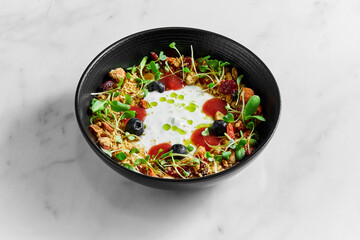 Healthy breakfast bowl of granola with dried fruits, berries, nuts, microgrin and yogurt on a light marble background
