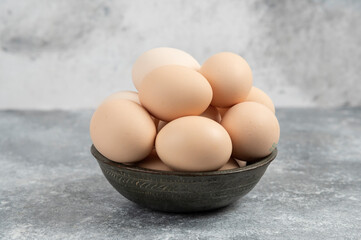 Dark bowl of fresh uncooked eggs on marble background