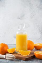 Glass pitcher of juice with fresh orange fruits on a wooden board