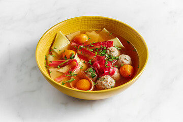 Chicken soup with noodles, yolks, and meatballs on a marble background