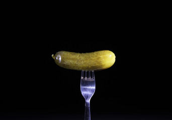 pickled cucumber on a fork. pickled vegetable on a black background. canned food.
