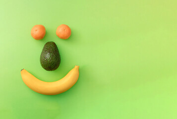 Positive smiley face from banana, avocado  and tangerine on a green background with copy space. Flat lay colorful concept.