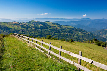 Fototapeta na wymiar Long wooden fence along a mountain road with a scenery hills landscape, Western Serbia. Bio stock-breeding and farming.