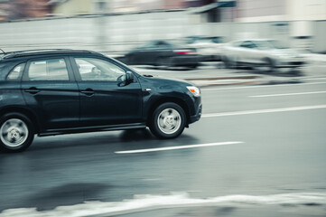 fast moving SUV rides on a winter city road. Side view of black car on wet slippery road in motion. Vehicle shot with blurred effect