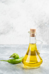 Green chili peppers with a bottle of extra virgin olive oil on marble background