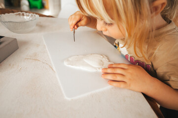 The hands of a small child who rolls out the clay to create a gift, a surprise for relatives and families. Child development, hobbies, clay hobby. Made by hands. Cozy home atmosphere.