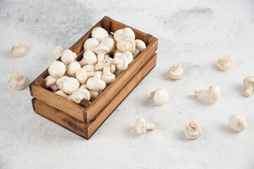 White mushrooms inside a wooden tray on a marble background