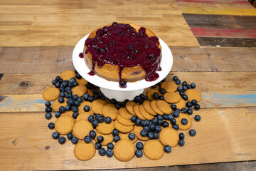A delicious blueberry and ginger biscuit cheesecake on a wooden kitchen work top surrounded by the ingredients used to create the cake