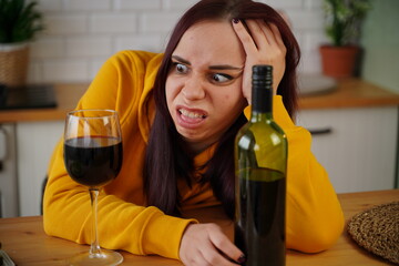 Unhappy young woman has headache from red wine. Adult female feels bad from alcohol while in kitchen.