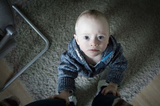 Toddler standing and holding the legs of his mother while looking up