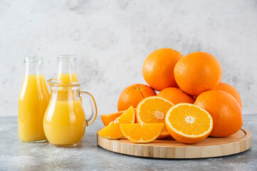 A glass pitcher of juice with fresh orange fruits on stone background