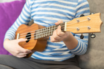 Woman playing Hawaiian guitar, sings a song on vintage ukulele at home. Selective focus. Close up