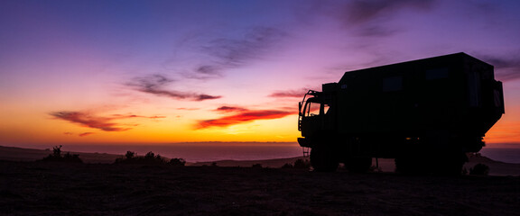 Silhouette of RV camping truck in front of colorful sunset, Sahara Desert, Morocco