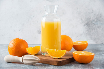 Glass pitcher of juice with fresh orange fruits on a wooden board